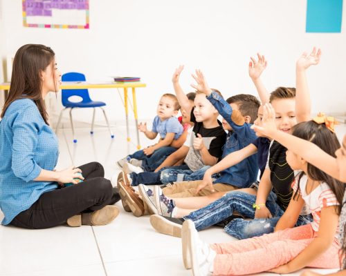 Profile view of a group of preschool students raising their hands and trying to participate at school